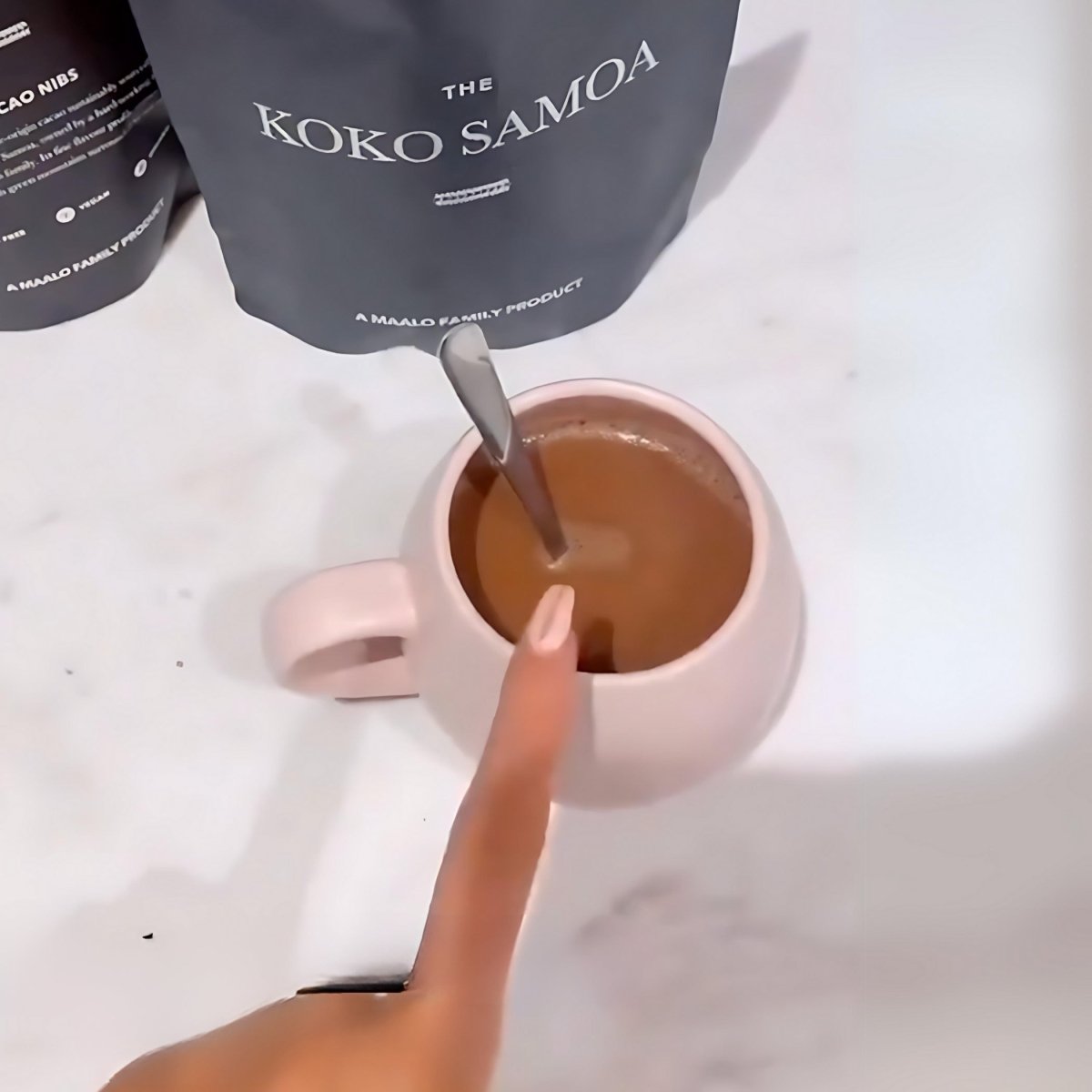 A cup of hot Koko Samoa instant drinking chocolate by THE KOKO SAMOA, served in a mug with a spoon on a cozy table.